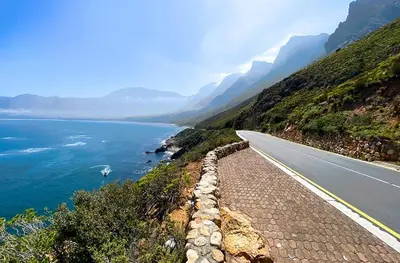 a road on the side of a mountain next to the ocean at Silvertree Collective Ocean and Mountain View in Bettyʼs Bay