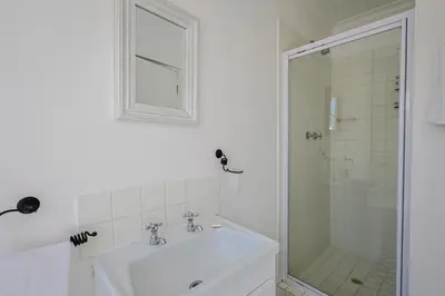 a white bathroom with a sink and a shower at Fully Equipped Claremont Home with Pool & Style in Cape Town