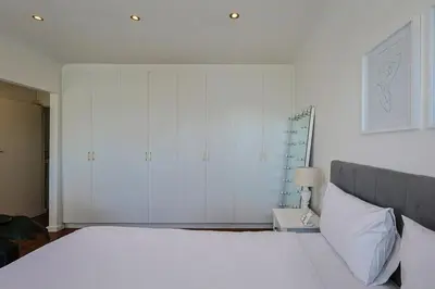 a bedroom with a white bed and white cabinets at Fully Equipped Claremont Home with Pool & Style in Cape Town