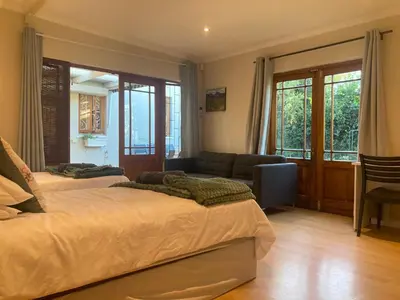 a bedroom with two beds and a couch and windows at Cozy garden Guest Suite in charming Claremont in Cape Town