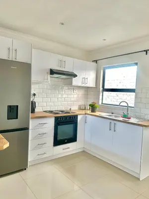a white kitchen with white cabinets and a window at Lalla Cottages - Cape Town in Cape Town