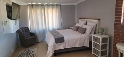 a bedroom with a bed and a chair and a television at Firehouse selfcatering Garden Cottage no 2 in Wellington
