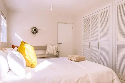 a white bedroom with a large bed with yellow and white pillows at Mimosa Voelklip Retreat in Hermanus