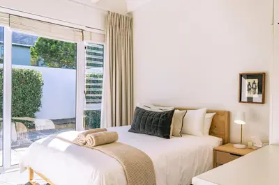a white bedroom with a bed and a window at Mimosa Voelklip Retreat in Hermanus