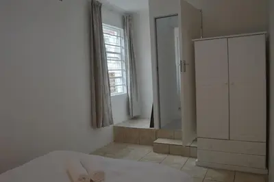 a white bedroom with a mirror and a bed at Oasis - Renovated - Queen extra length bed apartment in Cape Town