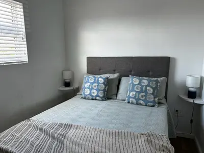 a bed with blue pillows in a white bedroom at BEACHees - cute central cottage in Kleinmond