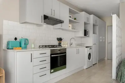 a white kitchen with white cabinets and a stove at Breeze of the Sea Apartment in Cape Town