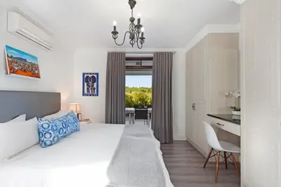 a white bedroom with a bed and a desk and a dining room at Winelands Golf Lodges 1 in Onder-Papegaaiberg