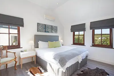 a bedroom with a bed and a chair and windows at Winelands Golf Lodges 1 in Onder-Papegaaiberg