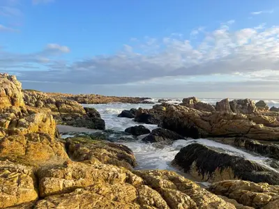 a rocky shoreline with the ocean and the waves at Barking Beach Cottage, Sandbaai - Pet Friendly in Hermanus