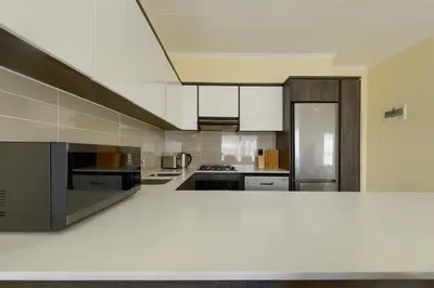 a large kitchen with white counters and appliances at Chic & Cozy Apartment with Pool, Gym & Balcony - The Sandown in Cape Town