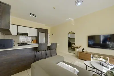 a living room and kitchen with a couch and chairs at Chic & Cozy Apartment with Pool, Gym & Balcony - The Sandown in Cape Town