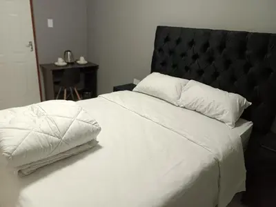 a bedroom with a white bed with a black headboard at Spring forth guest house in De Grendel