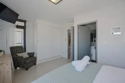 a white room with a bed and a chair at Aquarius 2 Bedroom Luxury Apartment in Cape Town