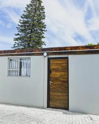 a white garage with a wooden door and a tree at Cedar Apartments on Century City in Cape Town