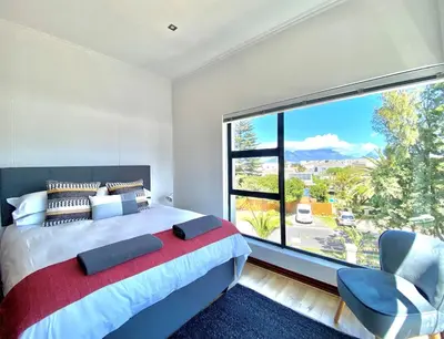 a bedroom with a large window and a bed and a chair at Peaceful 2-Bed Apartment in Boubergstrand in Cape Town