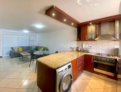 a kitchen with a washer and a living room at Peaceful 2-Bed Apartment in Boubergstrand in Cape Town