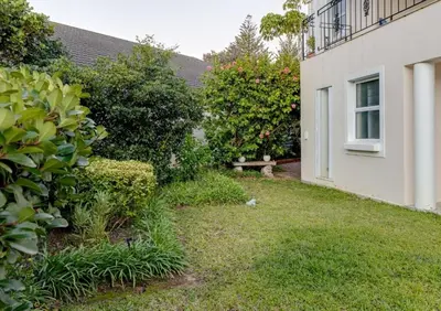 a yard next to a building with bushes and a window at Whale - a - While in Hermanus