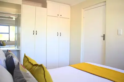 a bedroom with white cabinets and a bed at Tyger Classique Self-Catering Cape Town, Tyger Valley in Bellville