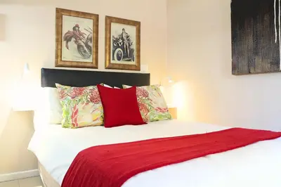a bed with a red blanket and two pictures on the wall at Tyger Classique Self-Catering Cape Town, Tyger Valley in Bellville