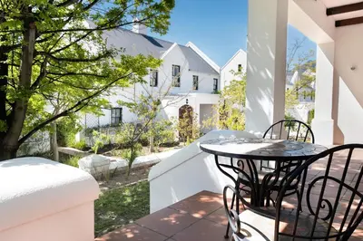 a table and chairs on a balcony with a house at Winelands Golf Lodges 13 in Stellenbosch