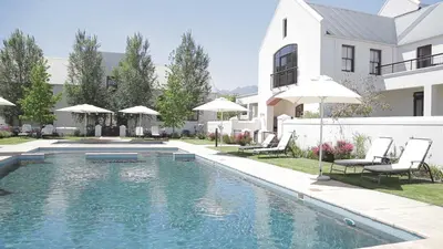 a swimming pool with chairs and umbrellas next to a house at Winelands Golf Lodges 13 in Stellenbosch