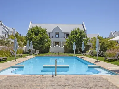 a pool with chairs and umbrellas in front of a house at Winelands Golf Lodges 22 in Stellenbosch