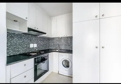 a kitchen with white cabinets and a washer and dryer at One Bedroom Loevenstein in Tygerberg Hills