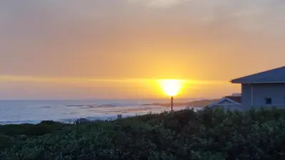 a sunset over the ocean with a house at Strandloper Apartments in Hermanus