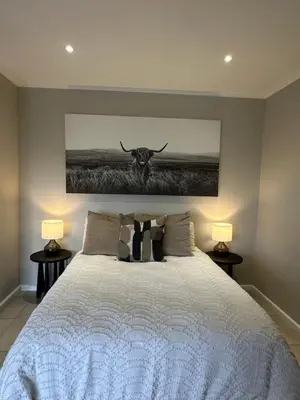 a bedroom with a white bed with a bull painting on the wall at Best Rest Somerset 3 in Somerset West