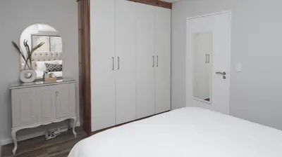 a bedroom with white cabinets and a bed with a mirror at Happy Days in Paarl
