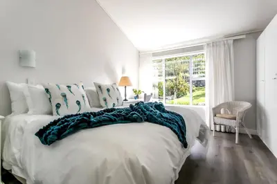 a white bedroom with a large bed with blue pillows at The Joyful Tortoise in Hermanus
