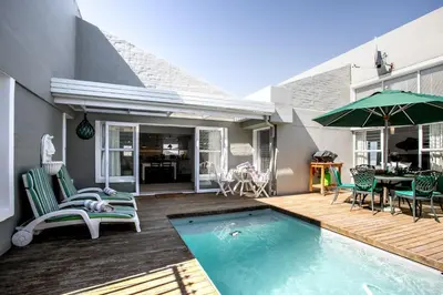 a house with a swimming pool with chairs and an umbrella at The Joyful Tortoise in Hermanus
