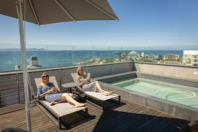 two women sitting on chairs next to a swimming pool at Mountain-View Studio - Hermanus Waterfront Apartments in Hermanus