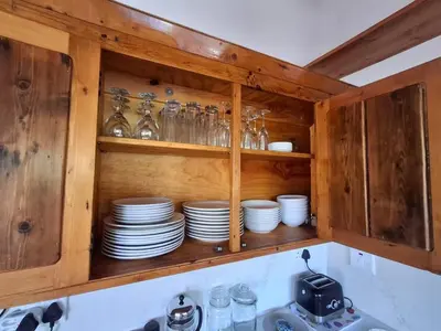 a wooden cabinet with plates and glasses in it at Alibi at the Sea in Bettyʼs Bay