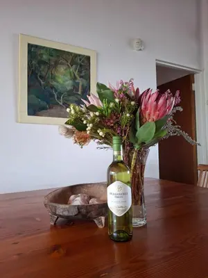 a bottle of wine and a vase of flowers on a table at Alibi at the Sea in Bettyʼs Bay