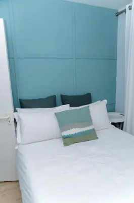 a bed with white pillows and a blue wall at Charming Self-catering Apartment in Gordonʼs Bay