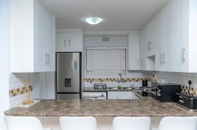a kitchen with white cabinets and a granite counter top at Charming Self-catering Apartment in Gordonʼs Bay