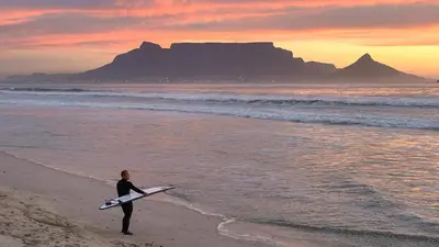 a person standing on a beach holding a surfboard at Luxurious Ocean View Beachfront Apartment in Cape Town