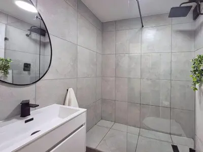 a bathroom with a shower and a sink and a mirror at Luxurious Ocean View Beachfront Apartment in Cape Town