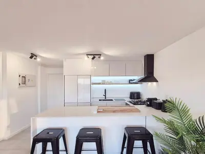 a kitchen with white cabinets and a counter with stools at Luxurious Ocean View Beachfront Apartment in Cape Town