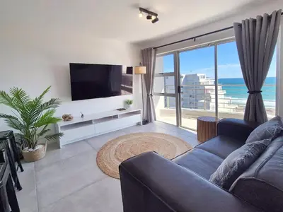 a living room with a couch and a large window at Luxurious Ocean View Beachfront Apartment in Cape Town