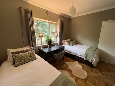 a bedroom with two beds and a desk with a window at The House Next Door in Stellenbosch