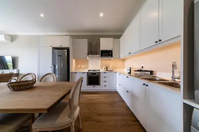 a kitchen with white cabinets and a wooden table at 68 LErmitage Elegant Mountain Apartment in Franschhoek