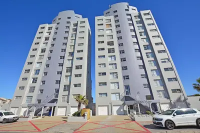 two tall white buildings with cars parked in front of them at SeeHUYS Boutique Bloubergstrand Beachfront Studio in Bloubergstrand