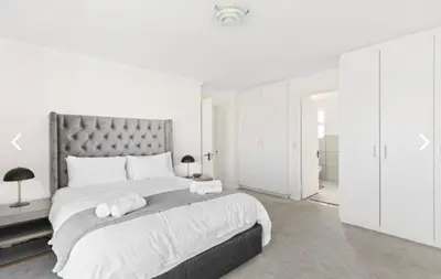 a white bedroom with a large bed with two towels at The Continental Sea Spray in Cape Town