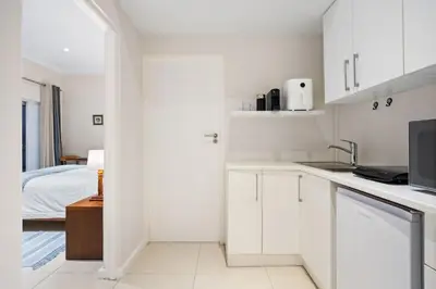 a white kitchen with white cabinets and a bed at Suikerbossie 52 in Cape Town