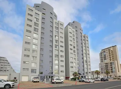 a large white building with cars parked in a parking lot at Ocean View B401 by CTHA in Bloubergstrand