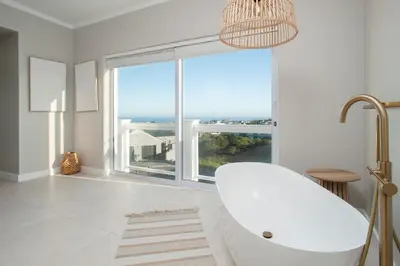 a white bathroom with a tub and a large window at Vermont Vista - With Pool in Hermanus