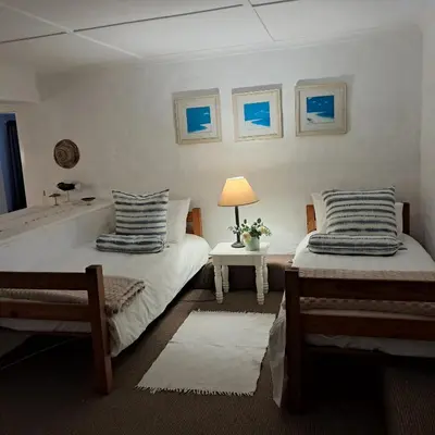 a bedroom with two beds and a table with a lamp at Vermont Garden Cottage in Hermanus
